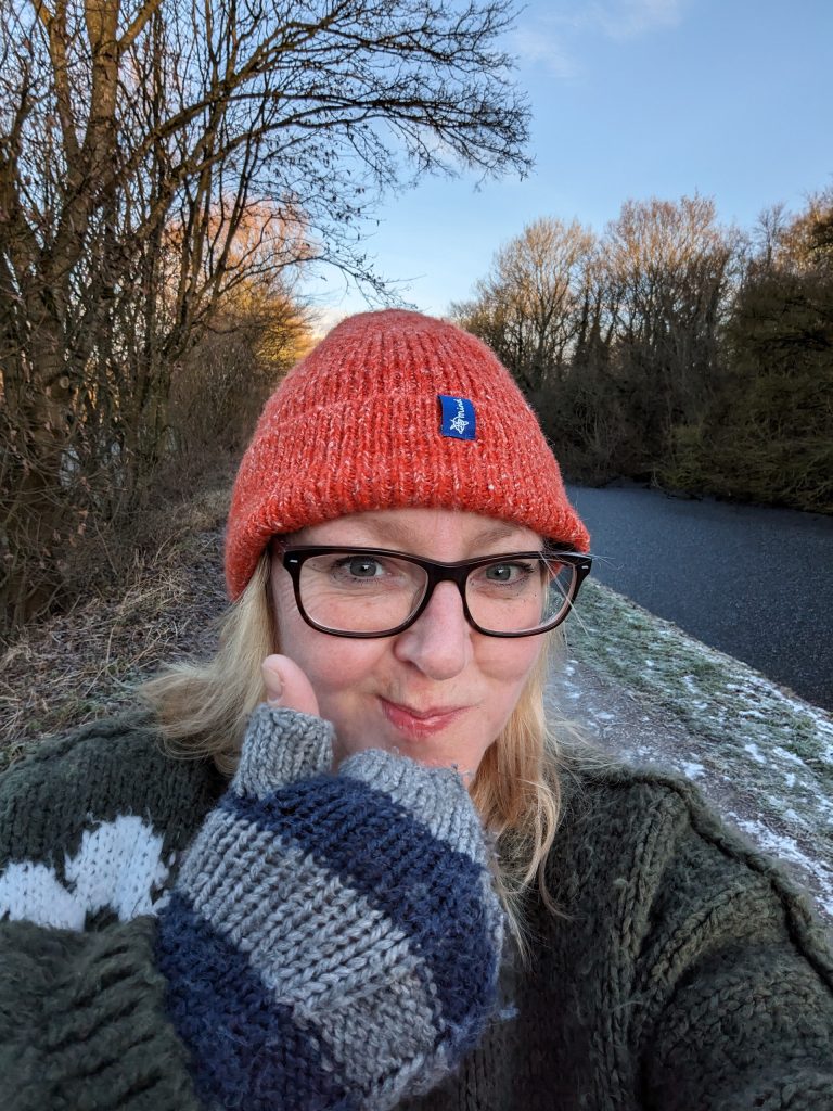 This is a picture of me walking beside a frosty canal, dressed in warm winter clothes. I'm wearing a hat supporting the charity MIND. It helps the viewer know a little more about me and who I am.
